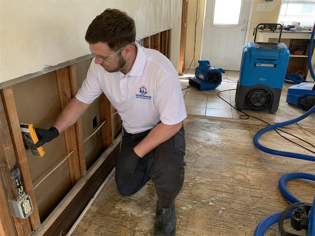 Technician using a moisture meter to inspect an opened wall after water damage