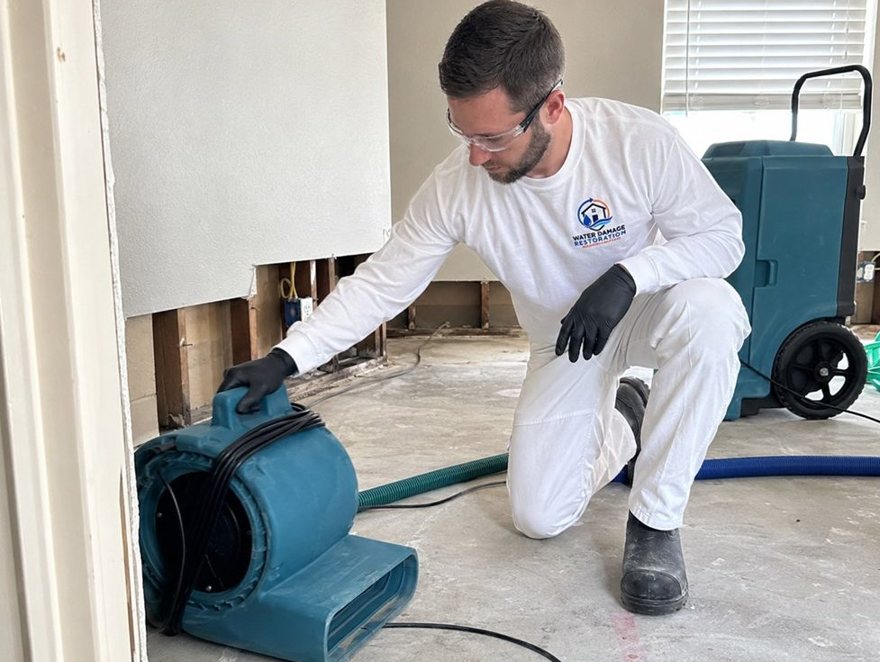 Water Damage Restoration Sacramento Rushline technician in a branded uniform positioning an air mover to dry a water-damaged room